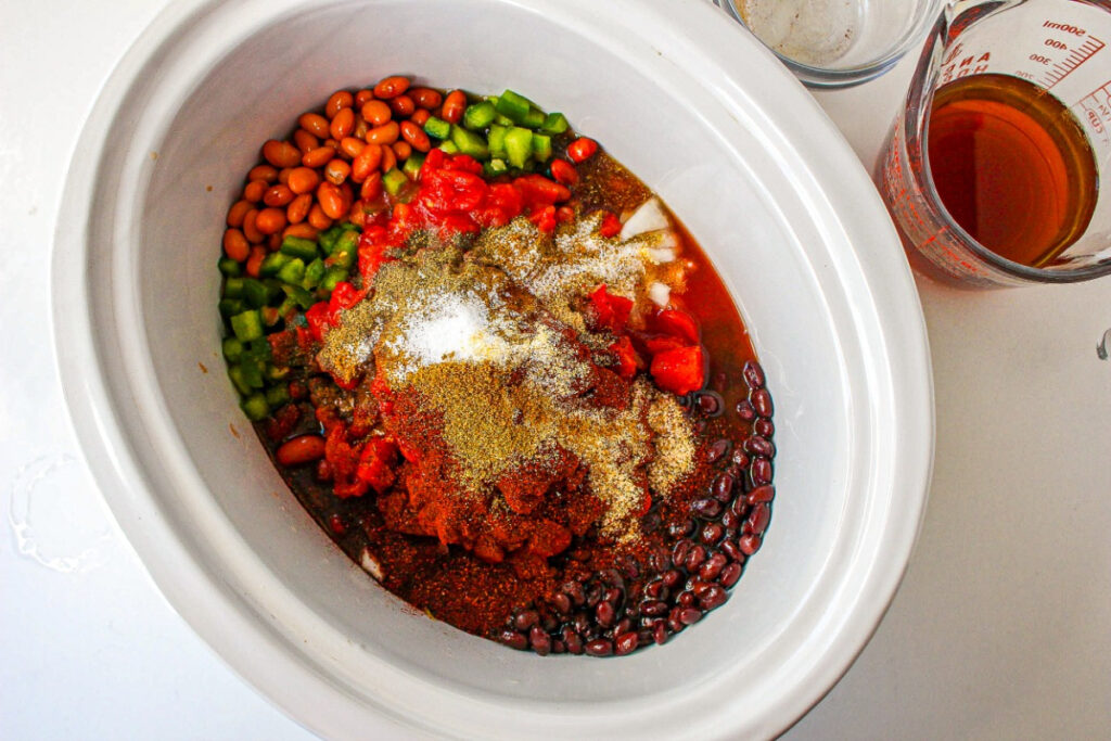 Ingredients with beans and spices added to slow cooker.