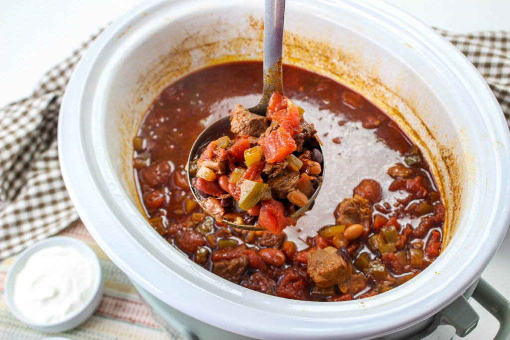 Chili in a slow cooker with a scoop of chili in the ladle. 
