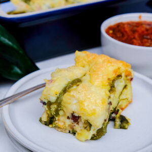 A slice of Chiles Rellenos on a white plate with a fork on the side of the plate.