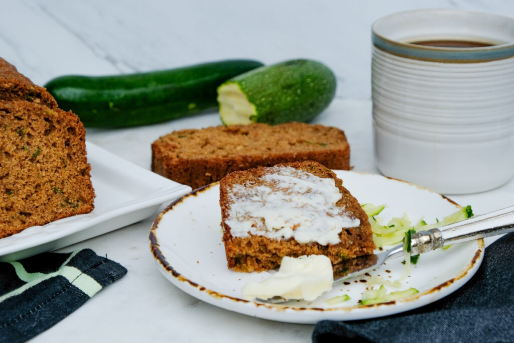 A slice of zucchini bread topped with butter on a small plate. 