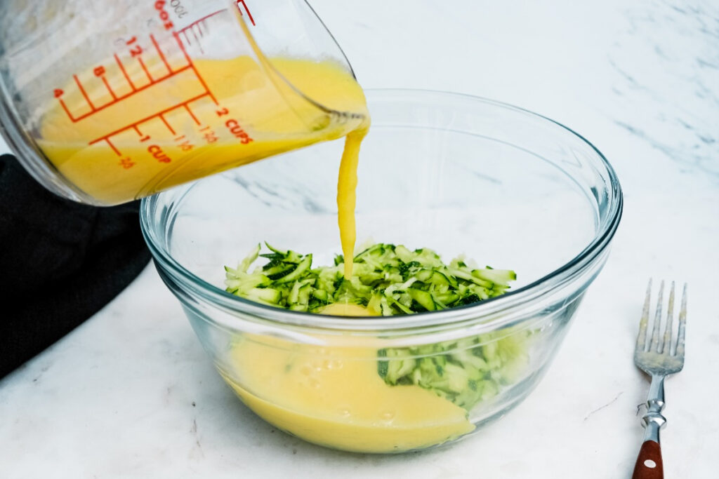 Egg wet mixture poured over the shredded zucchini in a clear mixing bowl. 