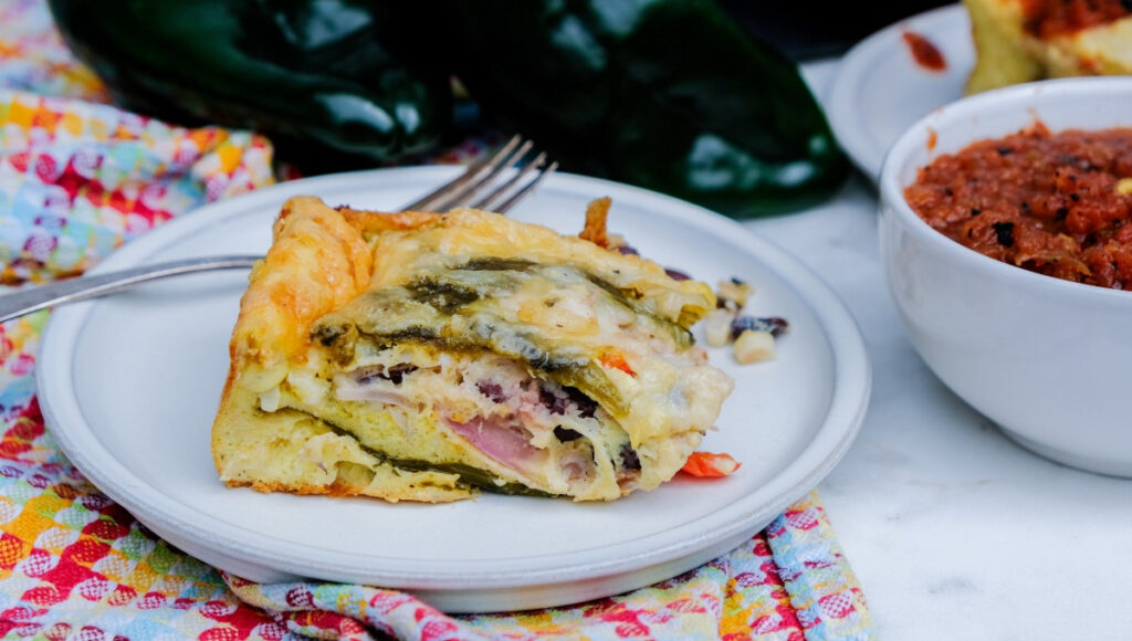 Slice of egg casserole on a white serving plate with salsa on the side. 