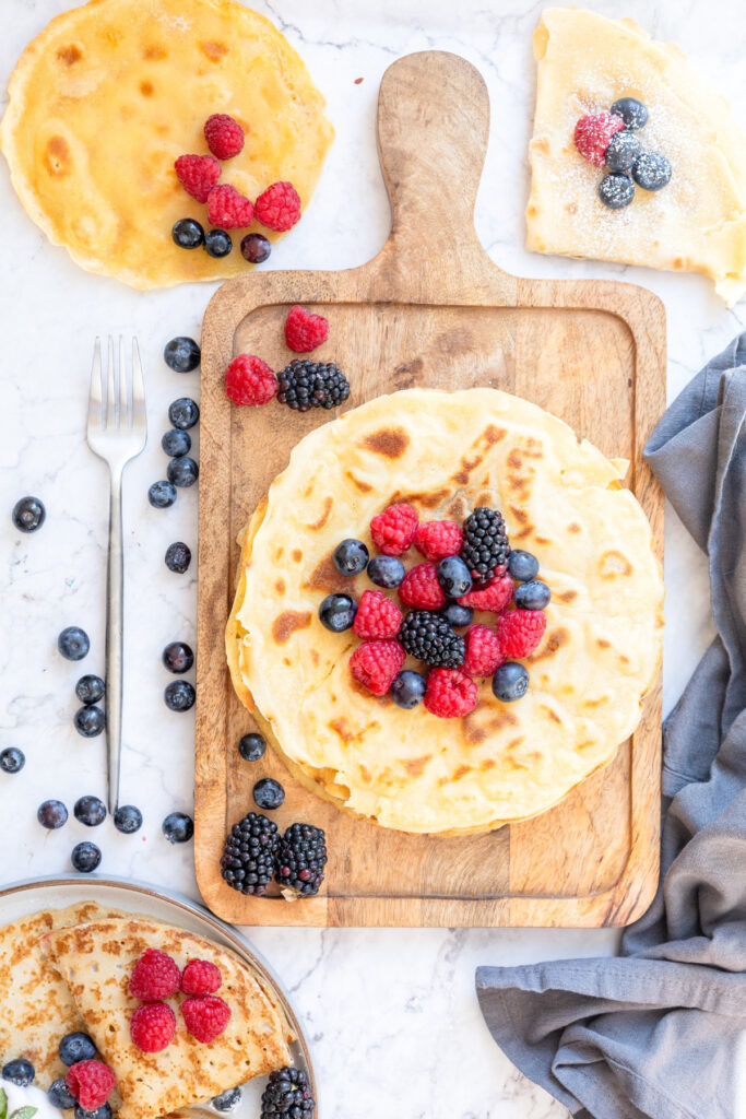 Top view of basic crepes on a brown cutting board topped with fresh berries.