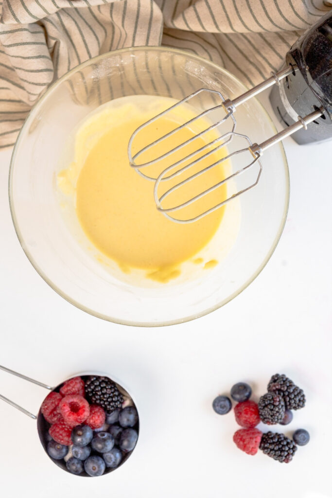 Crepe batter in a clear mixing bowl with an hand blender.