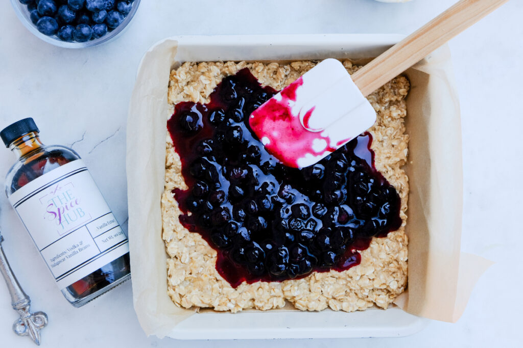 Adding blueberry sauce over oatmeal crust before cooking.