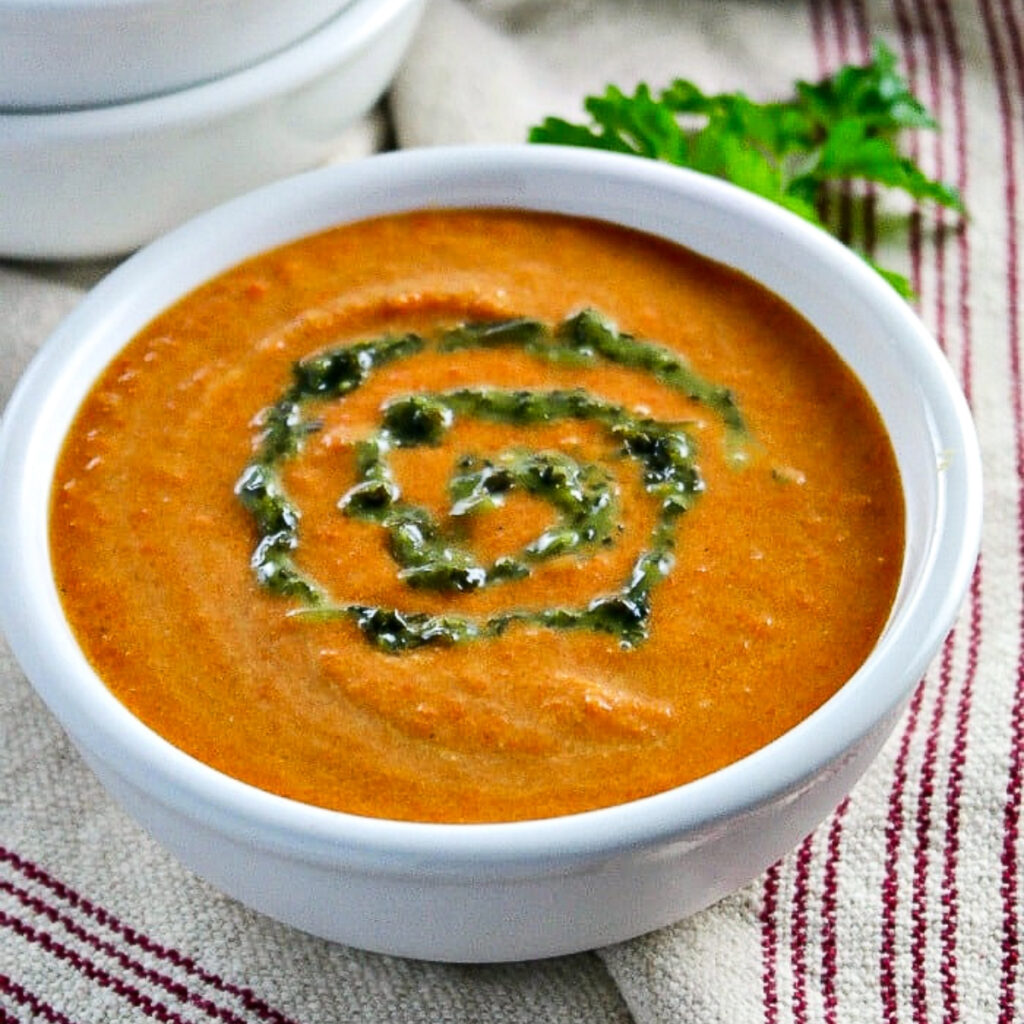 Vegan carrot curry soup with a swirl of cilantro puree in a white bowl.