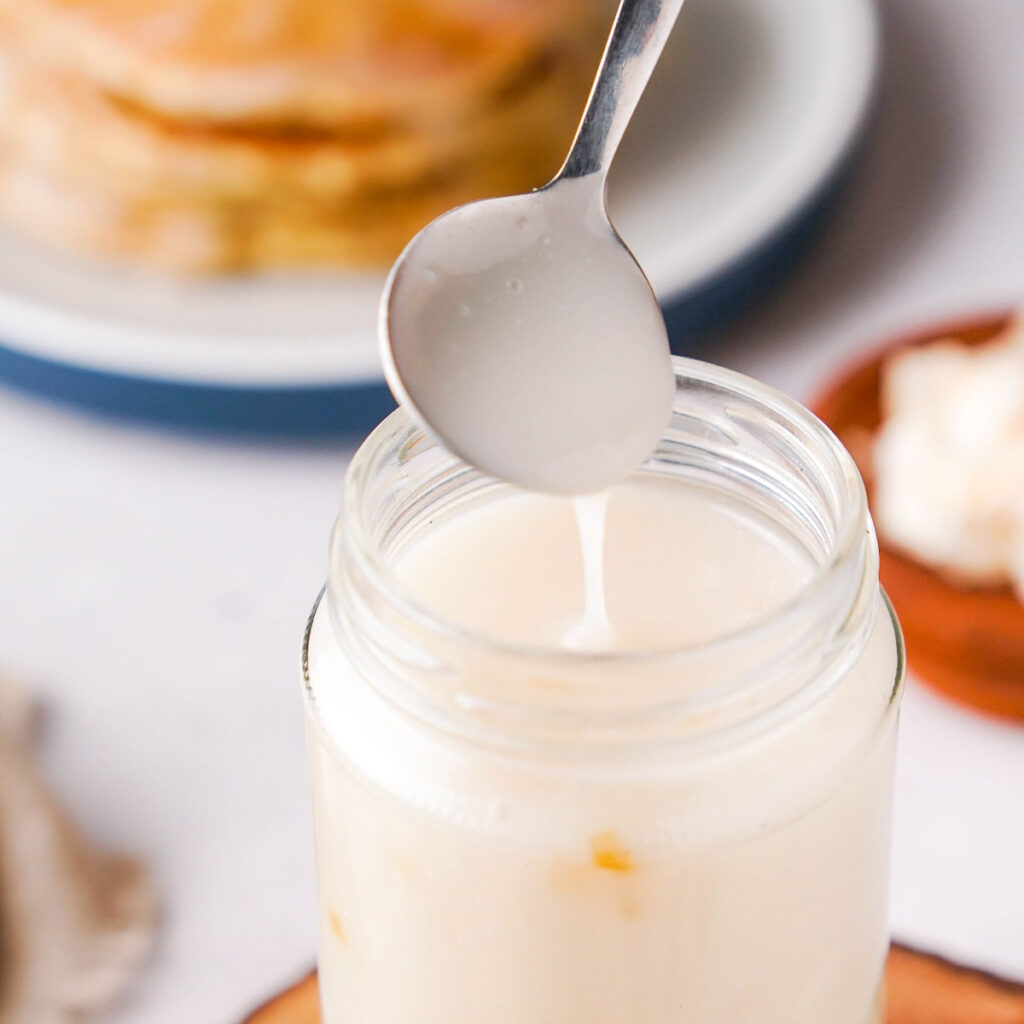 Homemade coconut syrup with a spoonful out of a clear glass jar.