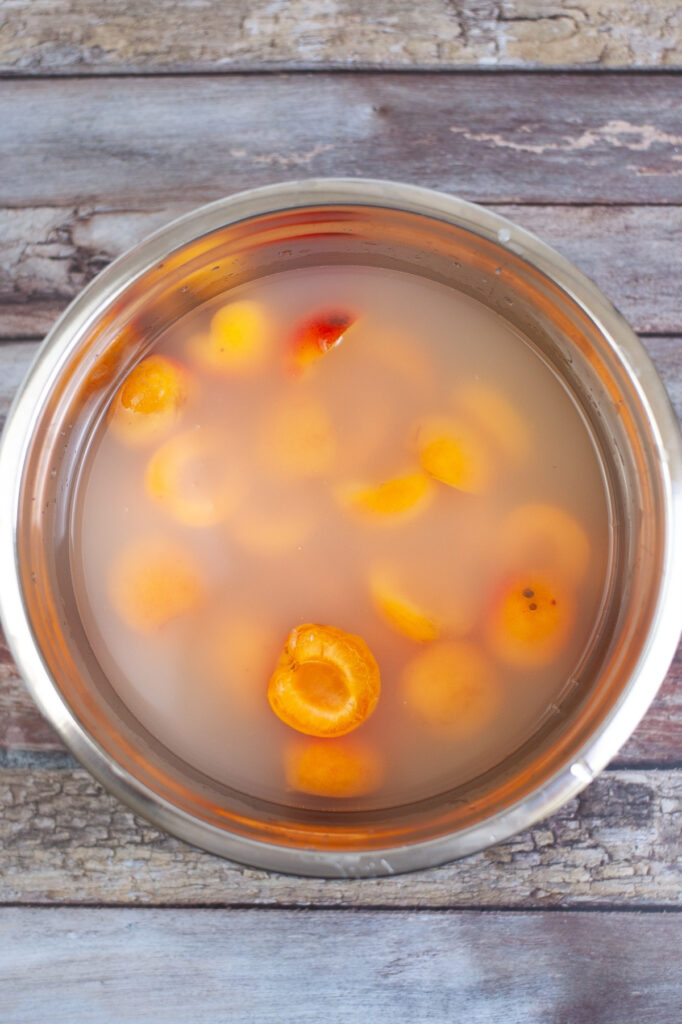 Apricots with lemon juice and water in a stainless steel bowl.