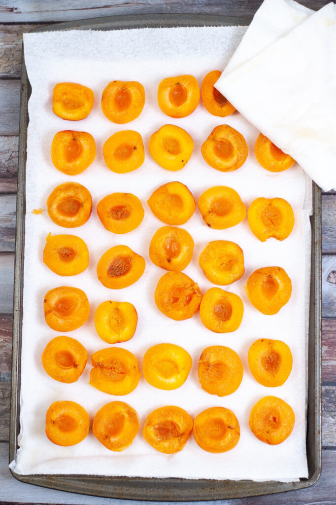 Sliced apricots on a baking sheet on paper towels.