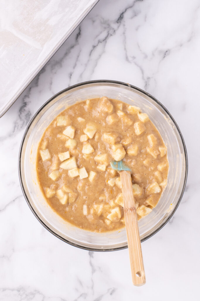 Cake batter with diced apples added to a mixing bowl. 