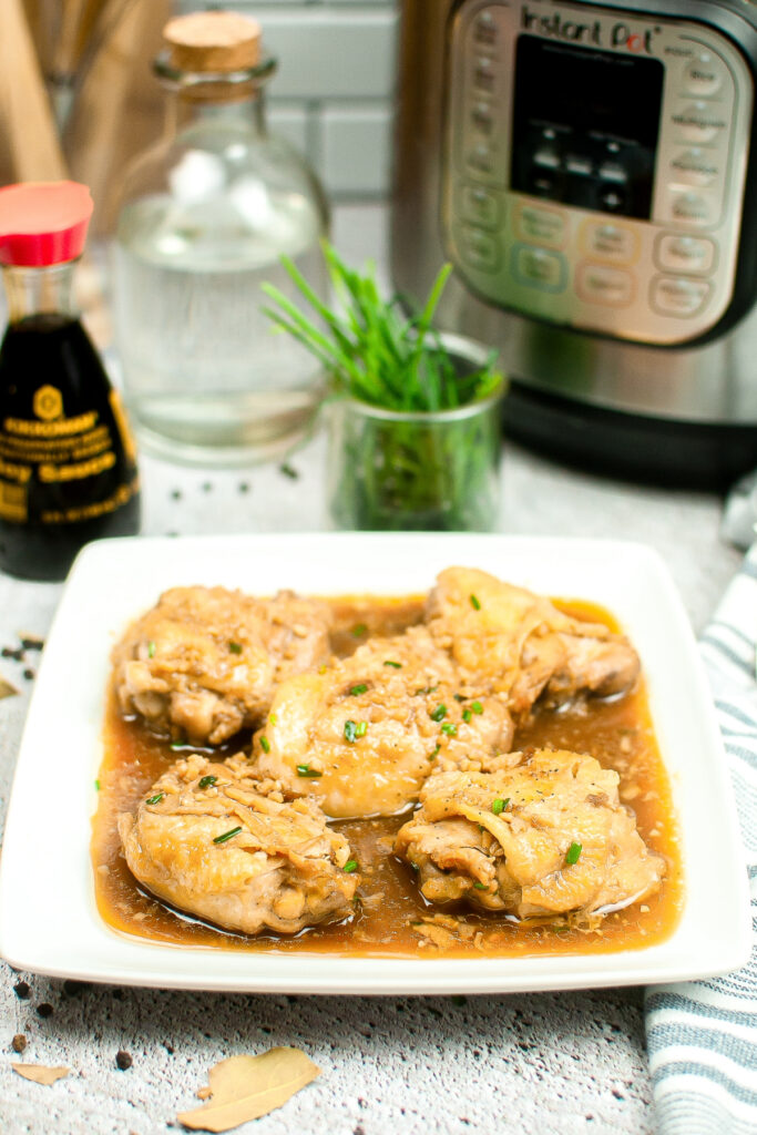 Chicken adobo on a white serving plate with an Instant Pot in the background. 