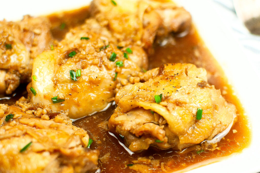 Cooked chicken adobo in a sauce on a white serving plate. 