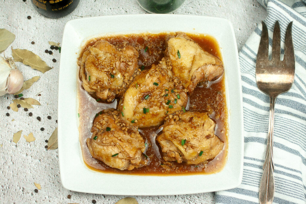 Cooked chicken on a serving plate with a silver serving fork on the side. 