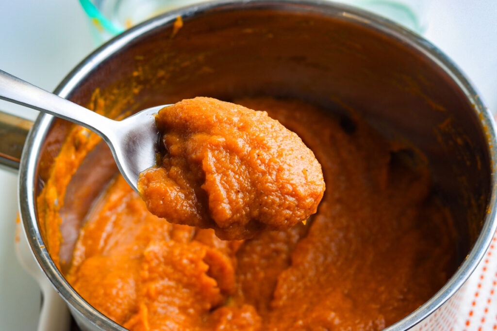 A spoonful of cooked pumpkin over a saucepan. 