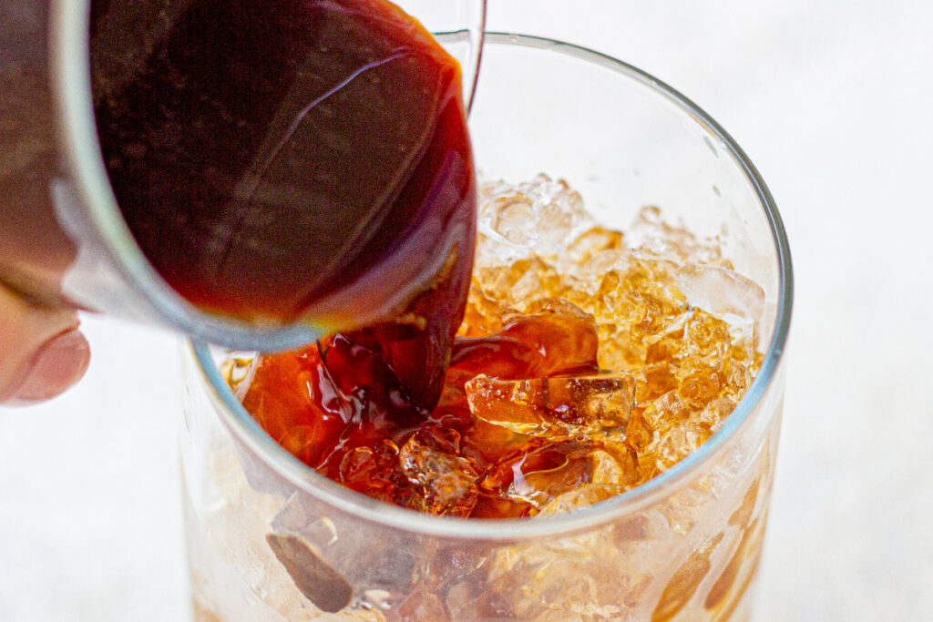 Pouring coffee concentrate into a clear glass with ice. 