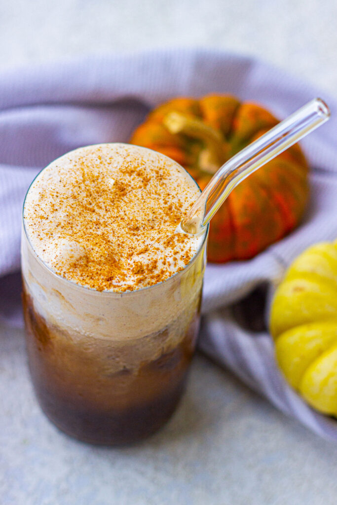 Iced coffee topped with whipped cream and cinnamon with a clear straw. 