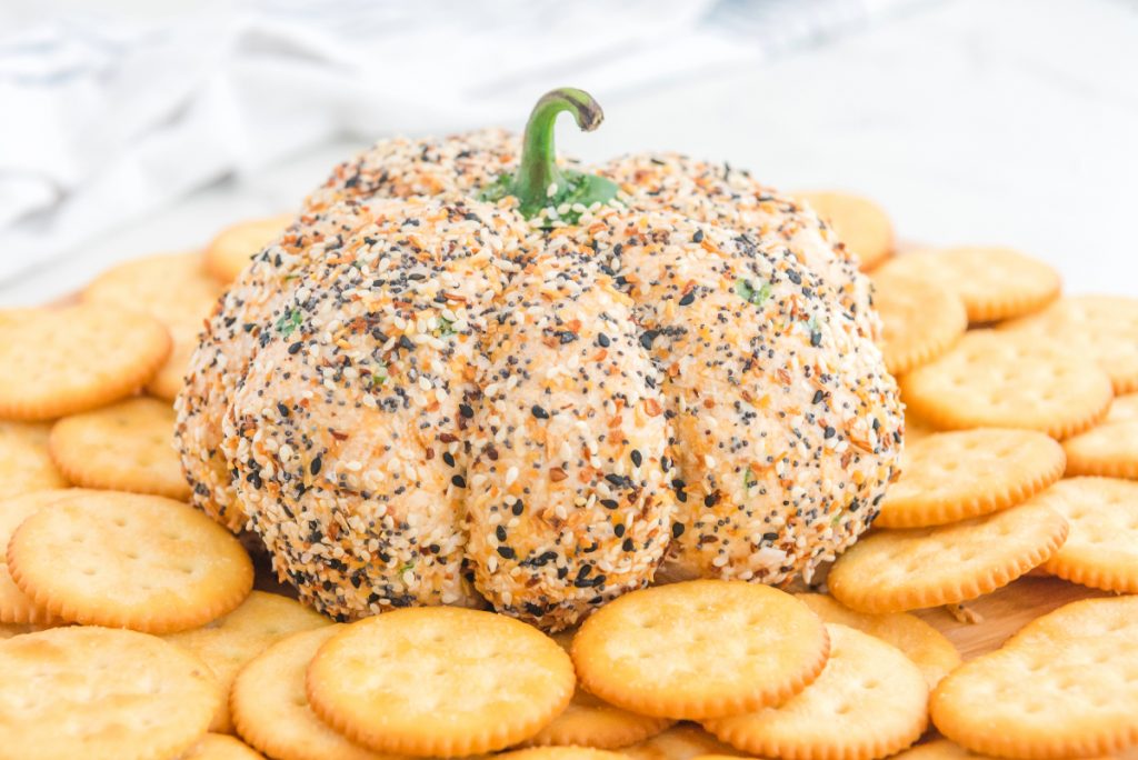 Cheese ball shaped into a pumpkin surrounded by crackers. 