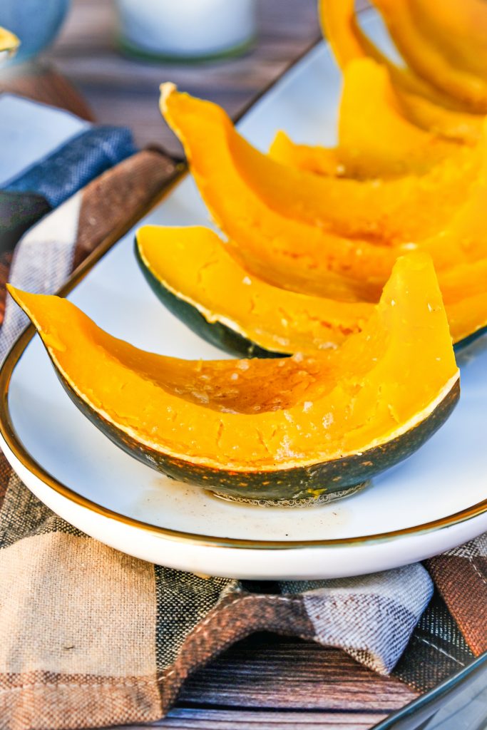 Cooked sliced acorn squash topped with brown butter on a white serving plate.