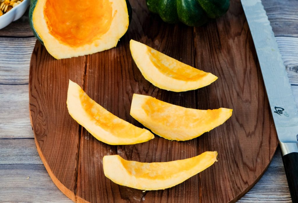 Acorn squash on a brown wood cutting board cut into wedges. 