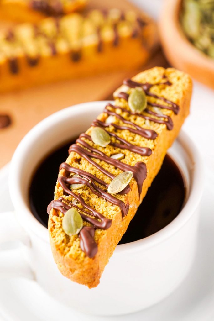 A white coffee cup with black coffee with a biscotti on top ready to enjoy. 