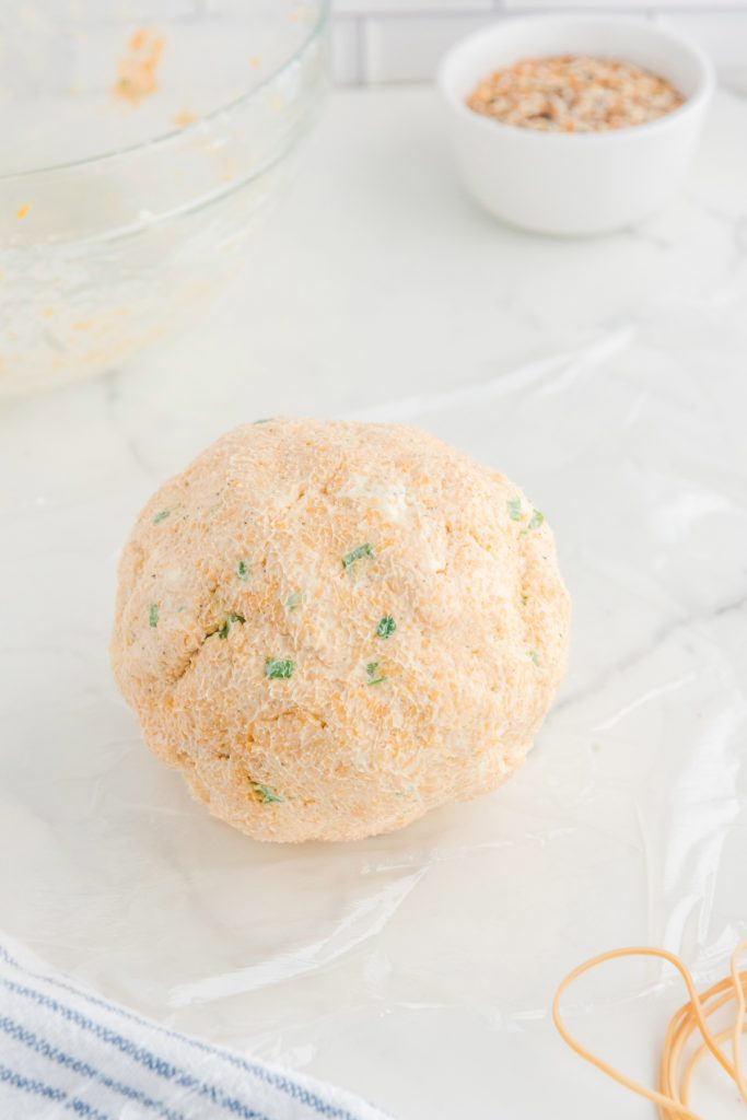 Cheese mix formed into a ball on a piece of plastic wrap. 