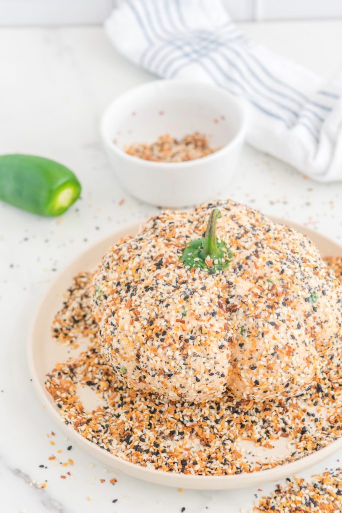 Pumpkin shaped cheese ball on a platter with everything bagel seasoning. 