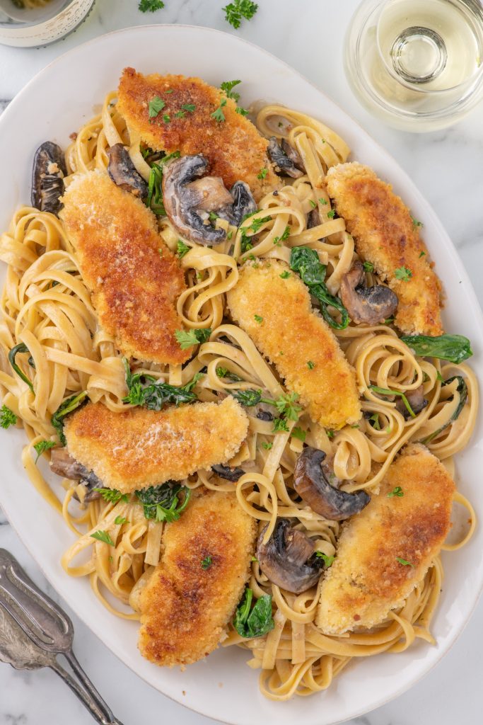 Top view of a white platter with chicken marsala over pasta.