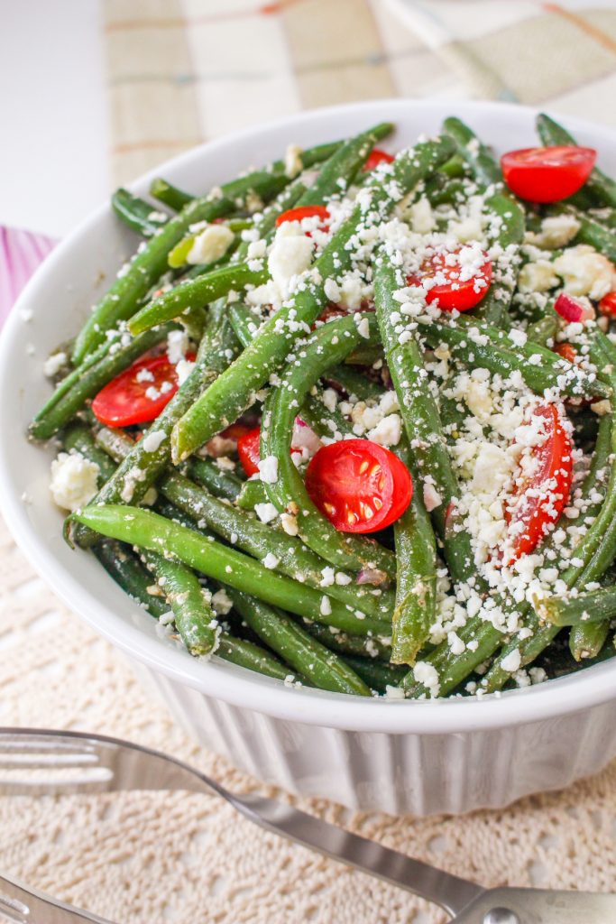 Green beans with feta cheese and cherry tomatoes in a white bowl.