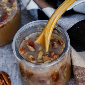 Homemade pecan maple syrup in a small clear glass serving jar.