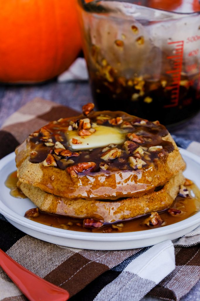 Syrup over waffles with pecans on a white serving plate. 