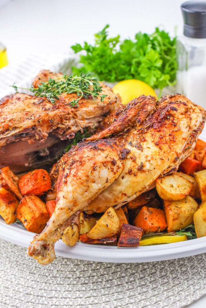 Roasted chicken and vegetables on a white serving platter. 