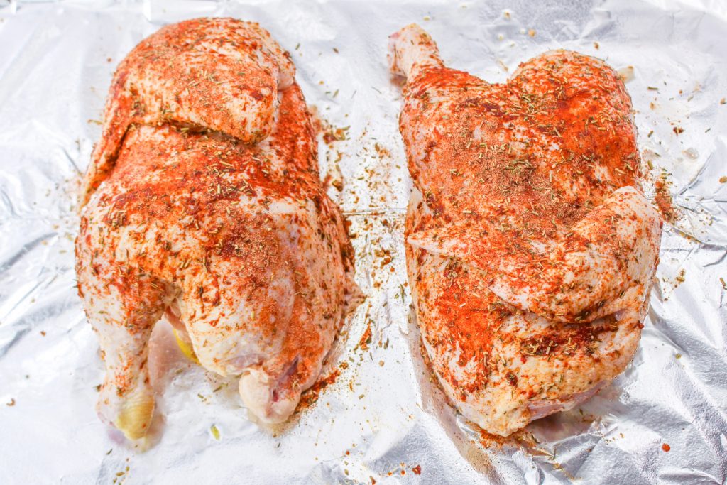 A chicken cut in half with seasoning on it before roasting in the oven. 