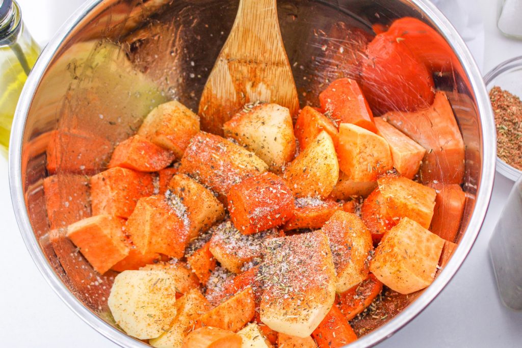 Diced root vegetables in a mixing bowl with spiced folded in the vegetable. 