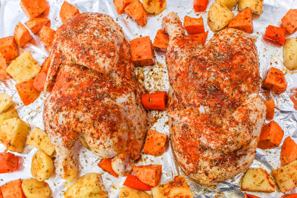 Half chicken and vegetables on a baking sheet before roasting. 