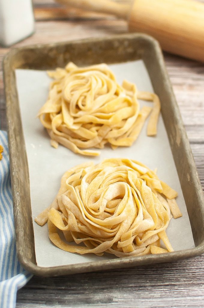 Homemade pasta sliced into fettuccini placed on a baking sheet before cooking. 