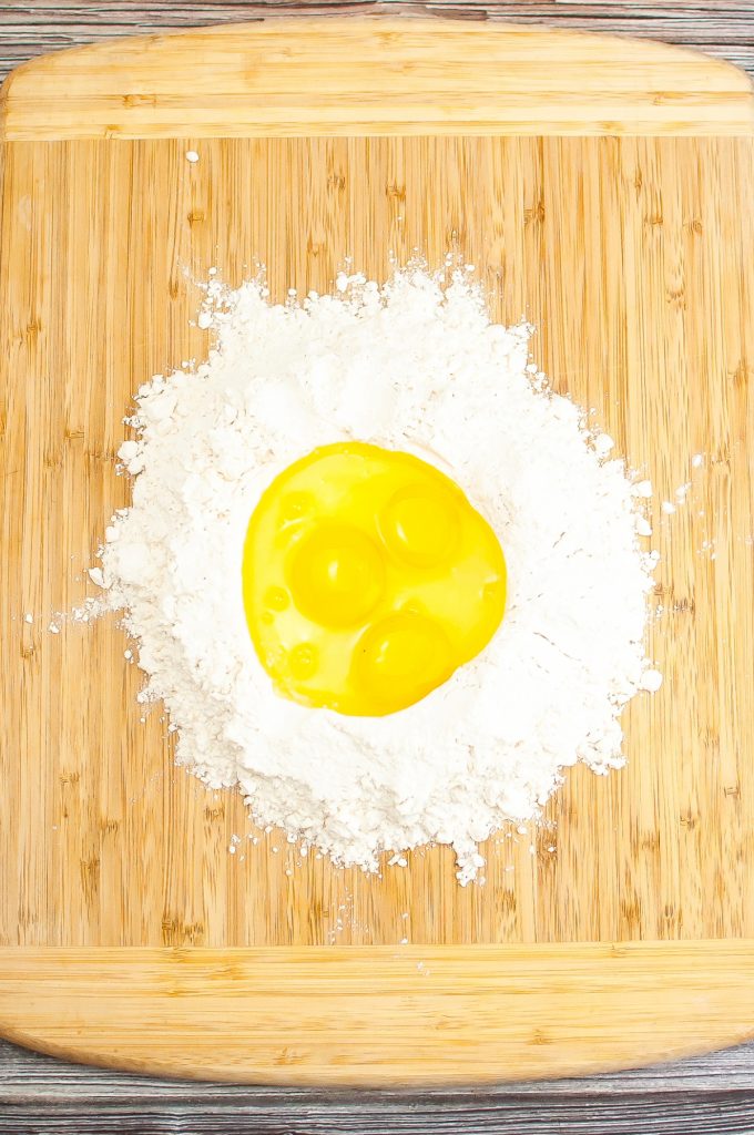 Flour on a cutting board with eggs in the center before mixing. 