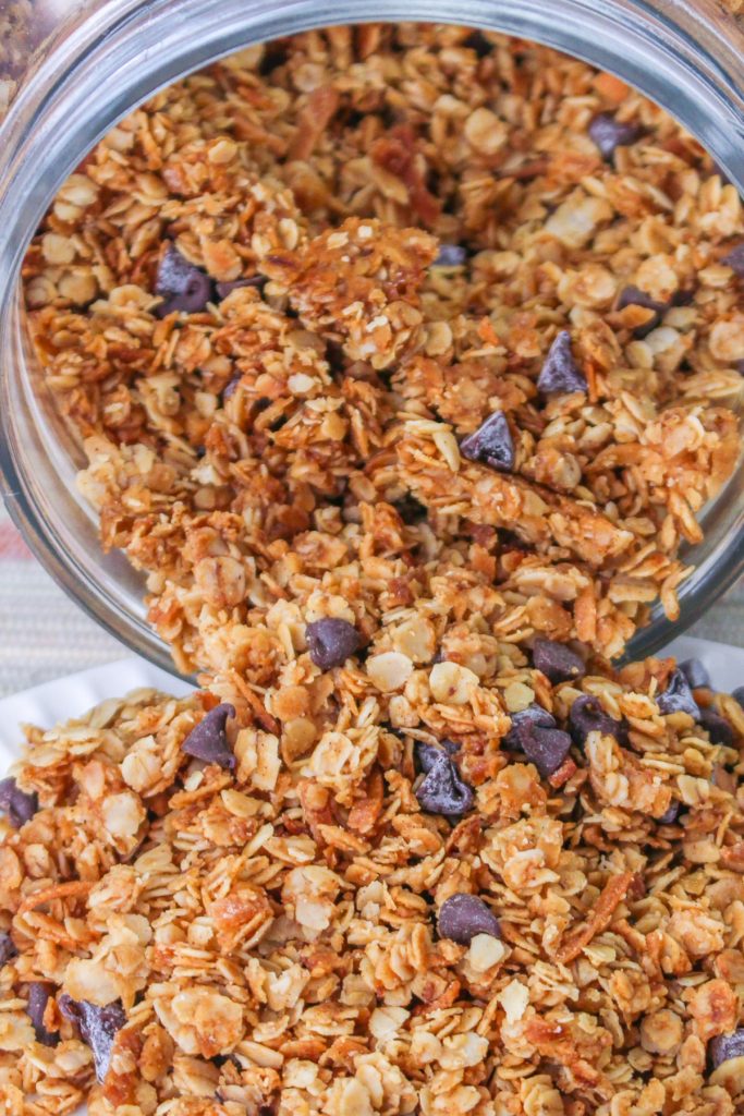 Homemade nut free granola with chocolate chips in a glass mason jar spilling onto a white plate. 