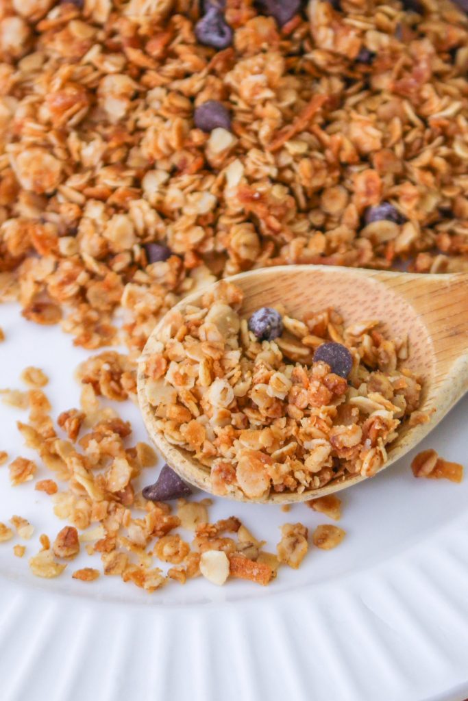 Homemade nut free granola on a white plate with a spoonful of granola on a wooden spoon. 