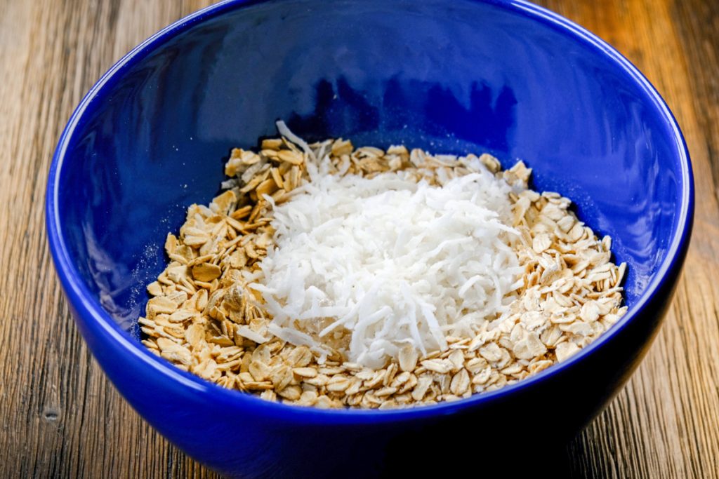 Old-fashioned oatmeal and coconut flakes in a blue mixing bowl.