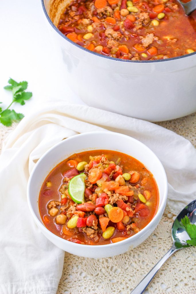 Chili in a white bowl with a white stockpot in the background. 