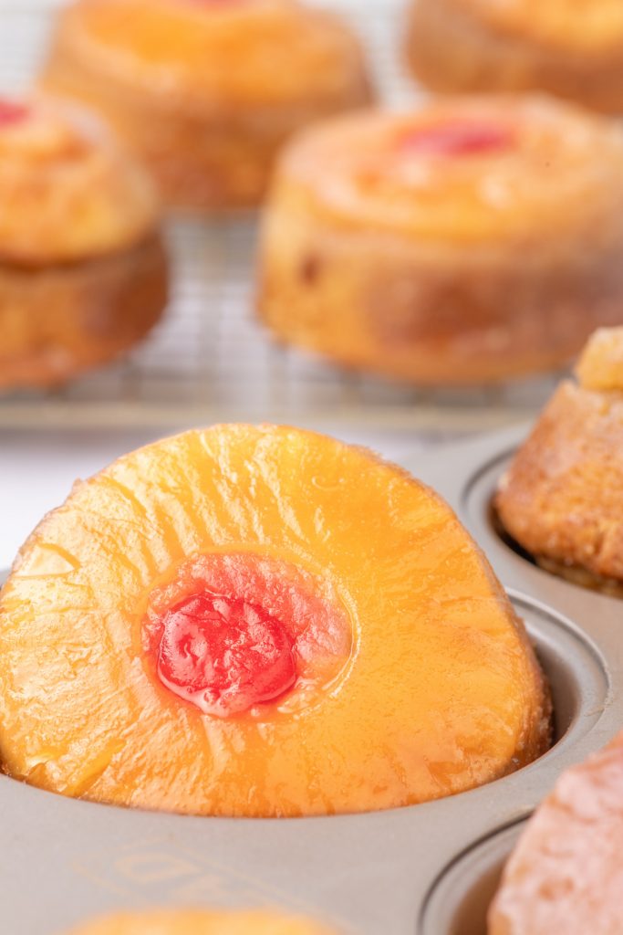 Pineapple upside down cupcakes in a muffin tin cooling before removing from the pan.