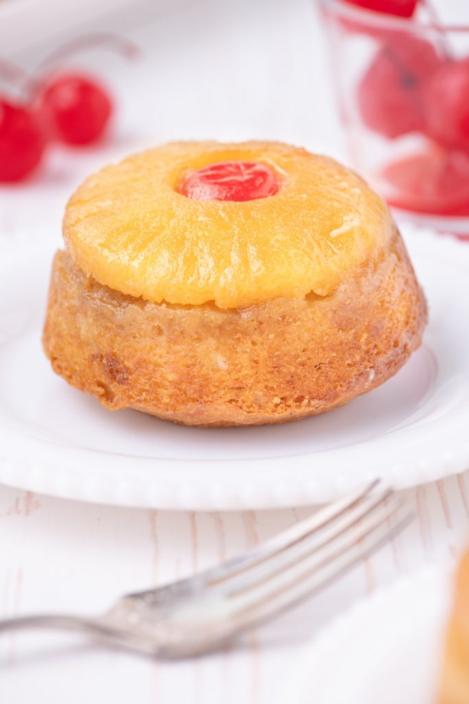 A pineapple upside down cupcake topped with pineapple and cherry in the middle.