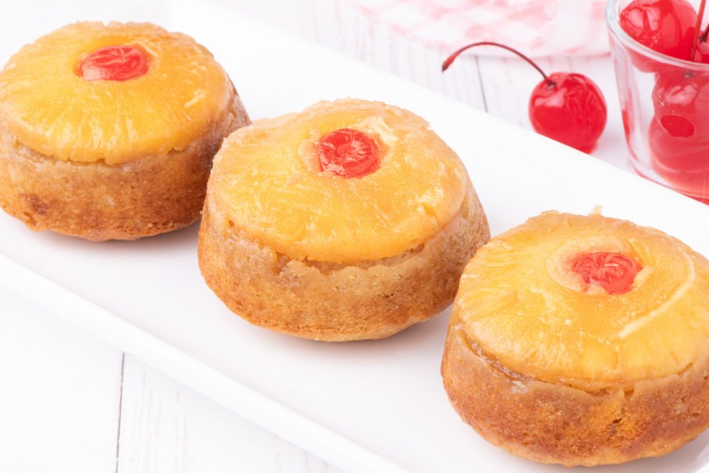 Pineapple upside down cupcakes on a white serving plate.