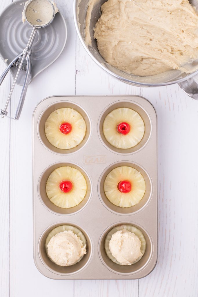 Adding batter to muffin tin over pineapple slices. 