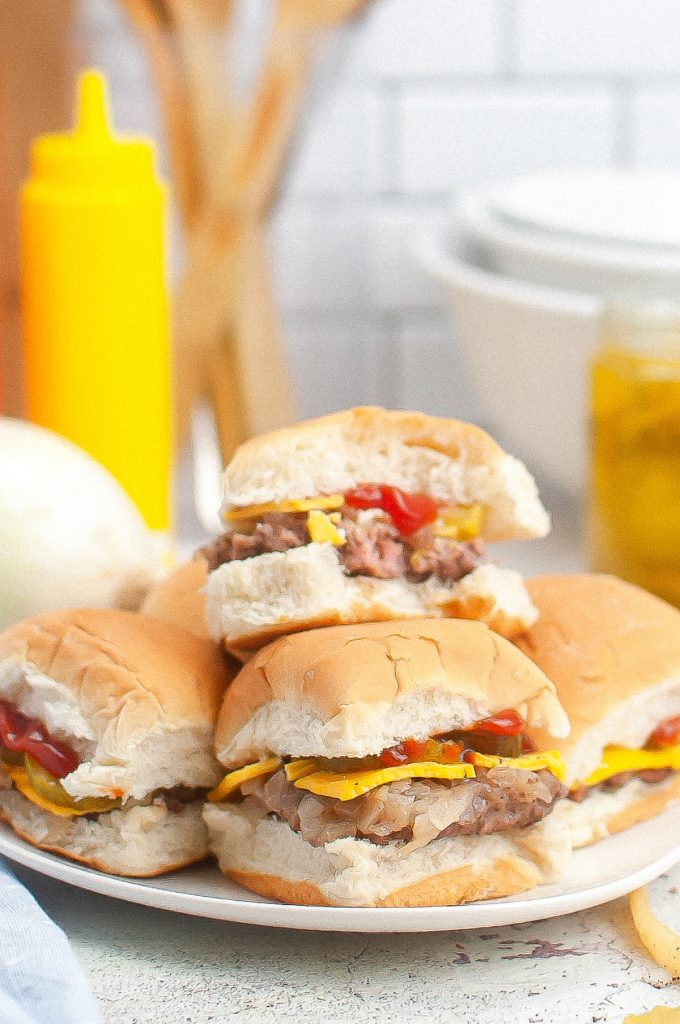slider hamburgers with cheese and catsup on a white plate.  