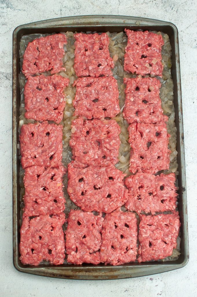 Hamburger sliders over diced onion on a baking sheet.