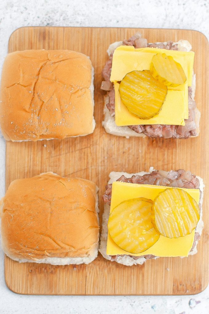 Assembling copycat White Castle Sliders with cheese and pickles on a cutting board. 