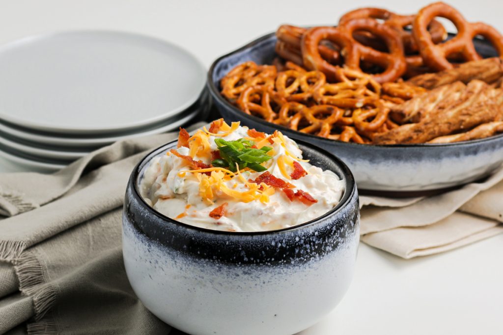 Appetizer dip in a small bowl with pretzels in the background. 