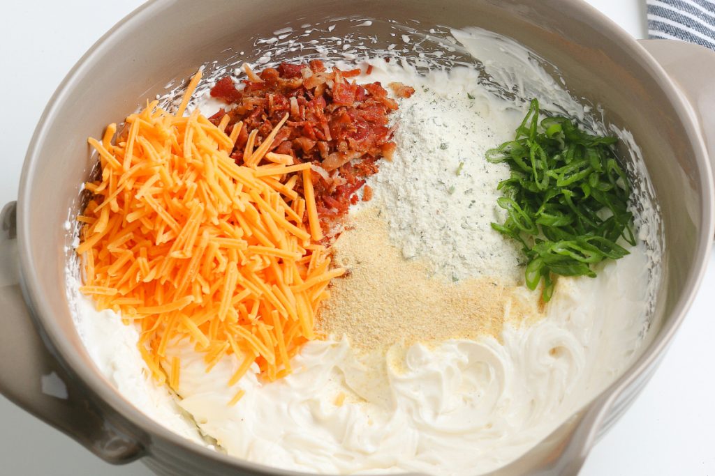 Spices and shredded cheese in a cream cheese mixture for homemade crack dip. 