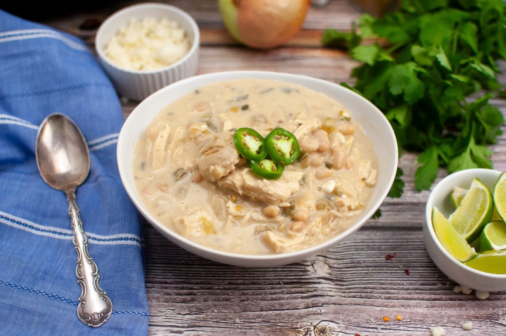 A dinner setting with a bowl of soup with a silver spoon on the side. 